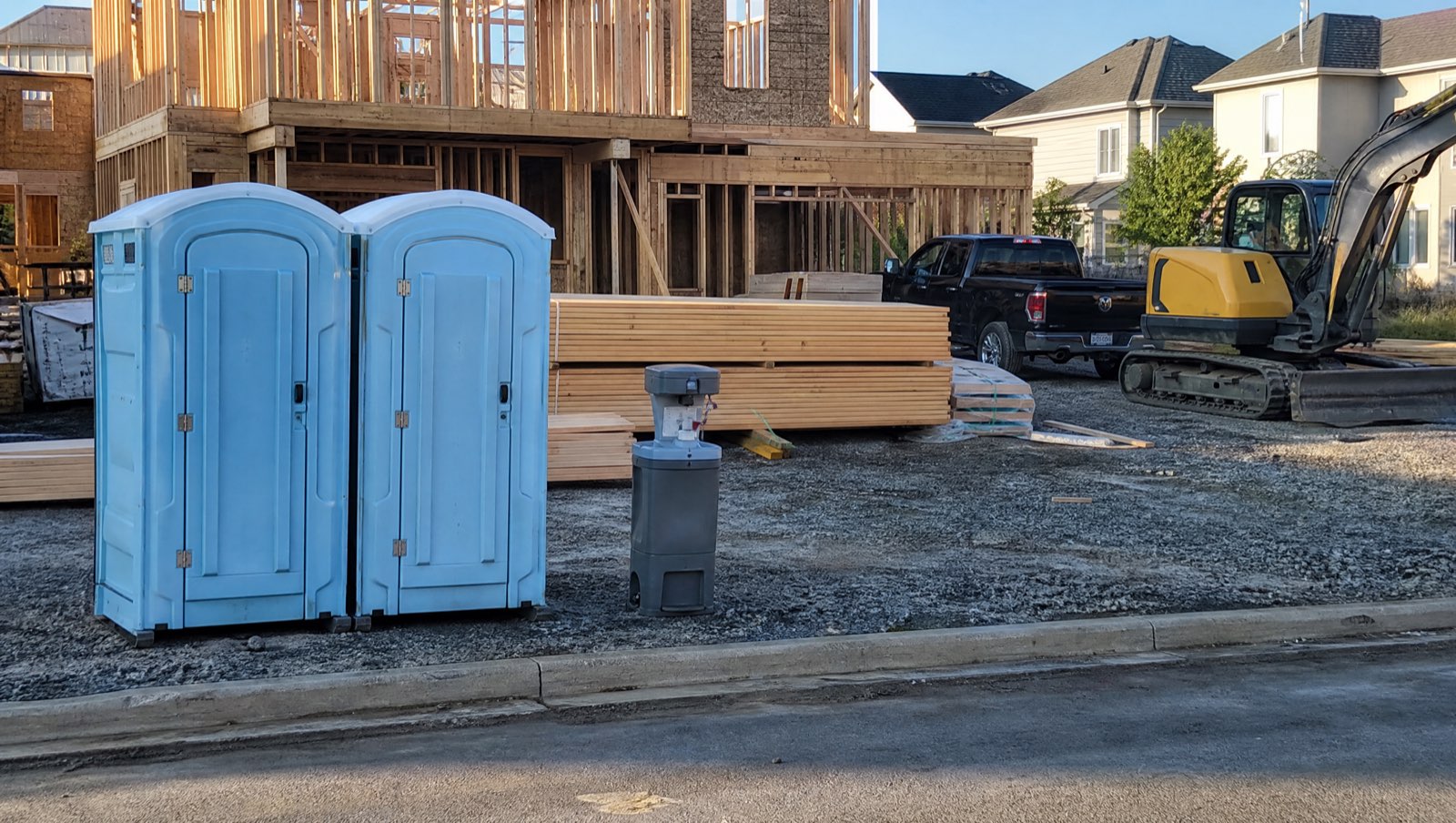 Two portable toilets and a hand wash station at a residential framing site